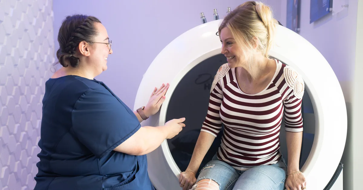 Client sitting in the OxyHealth Fortius 420 hard-shell hyperbaric chamber with a provider at iCRYO Grosse Pointe, MI
